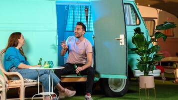 A teal van with a door open, a small table with drinks, and a potted plant.
