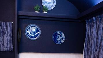 A room with a dark blue wall, a white cushioned bench, and two blue ceramic plates with designs.