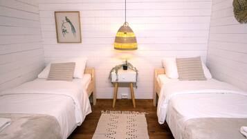 A room with two single beds, a hanging lamp, a small table with a plant, and a framed picture on the wall.