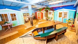 A beach-themed room with a wooden boat, a dining table, and colorful beach huts. - Outside Inn (Amsterdam-Duivendrecht)