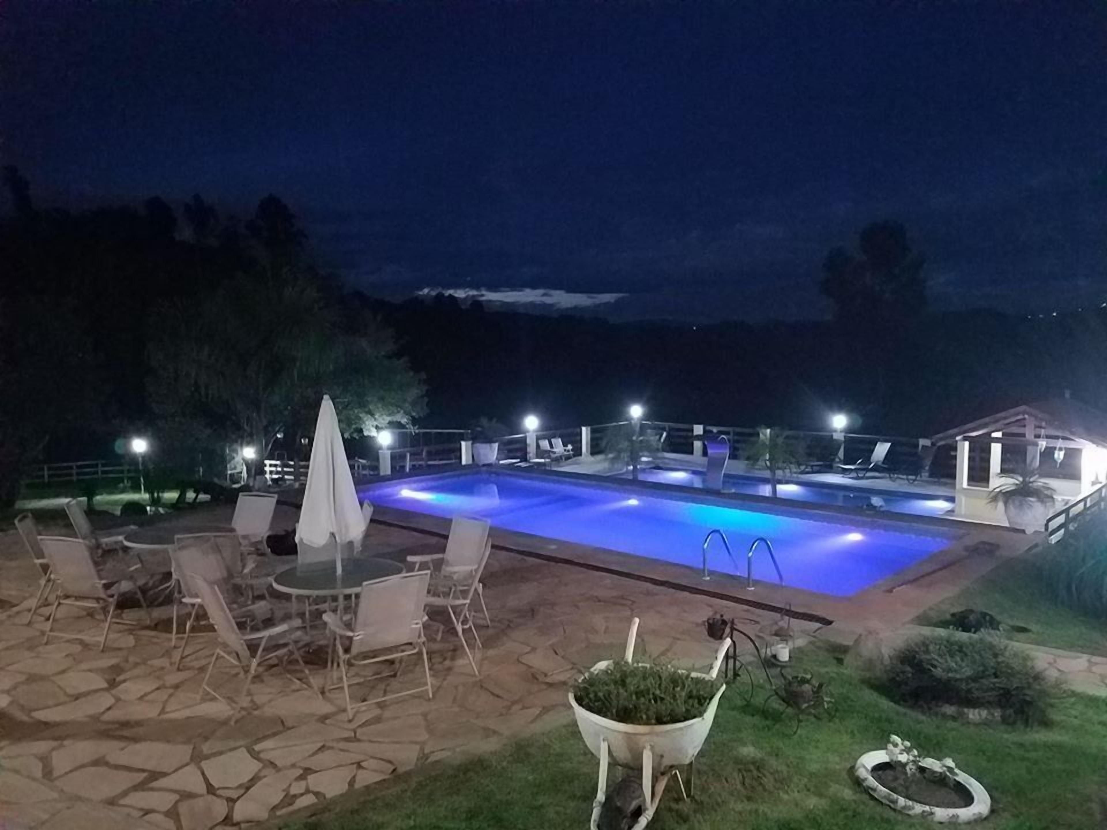 An outdoor swimming pool area with lounge chairs and a table, surrounded by stone tiles and potted plants.