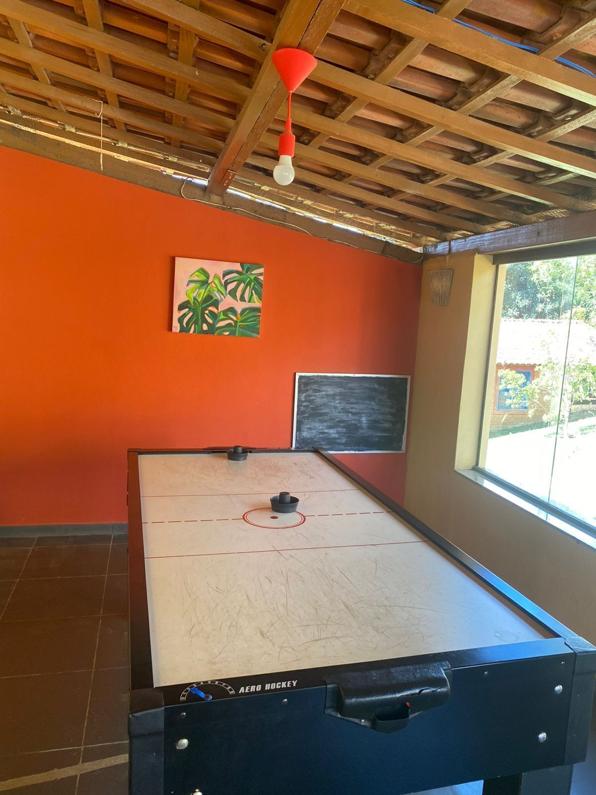 A room with a foosball table, a chalkboard, and a window with a view of greenery.