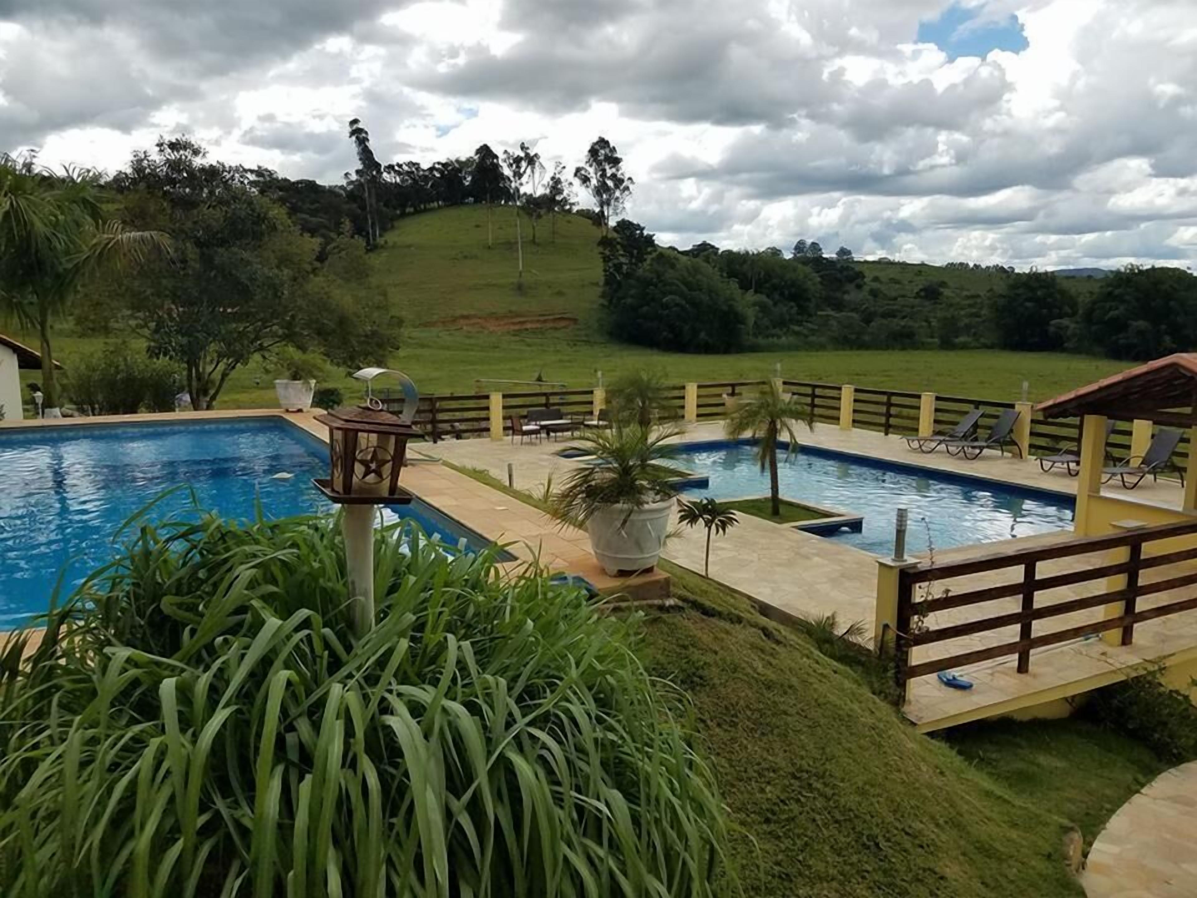 A swimming pool with a wooden deck, surrounded by lush greenery and a hill in the background.