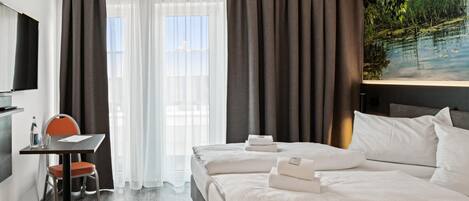 A hotel room with a bed, a desk with a chair, a TV, and a painting of a landscape.