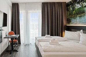 Habitación de hotel con dos camas, un escritorio con silla, televisión y un cuadro de un paisaje natural.