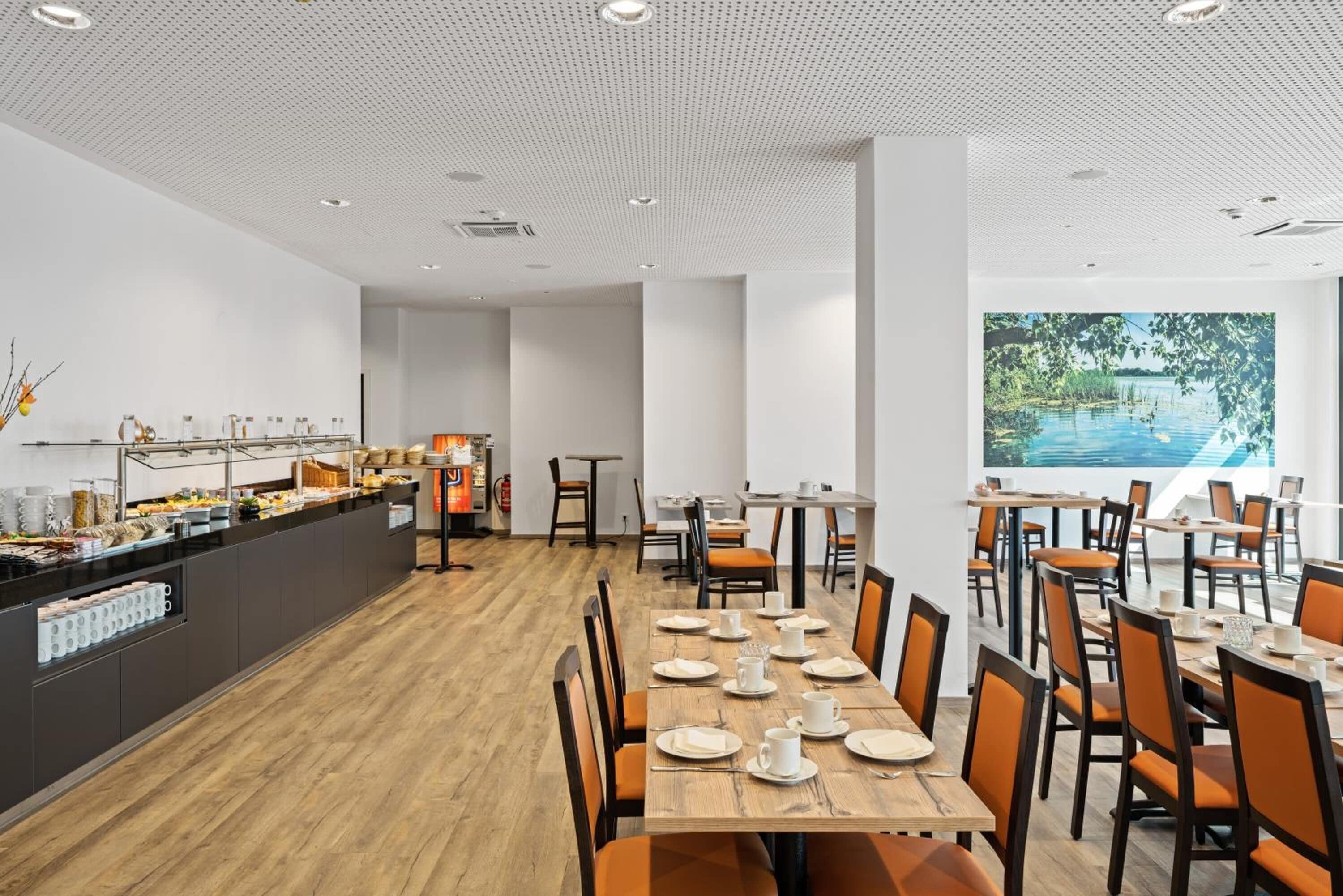 A spacious dining area with a long wooden table set for a meal, surrounded by orange chairs.