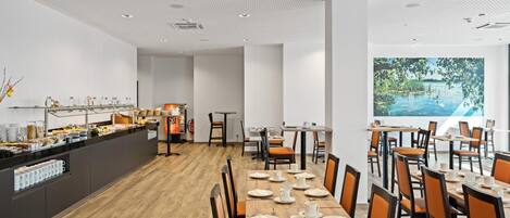 A spacious dining area with a long wooden table set for a meal, surrounded by orange chairs.