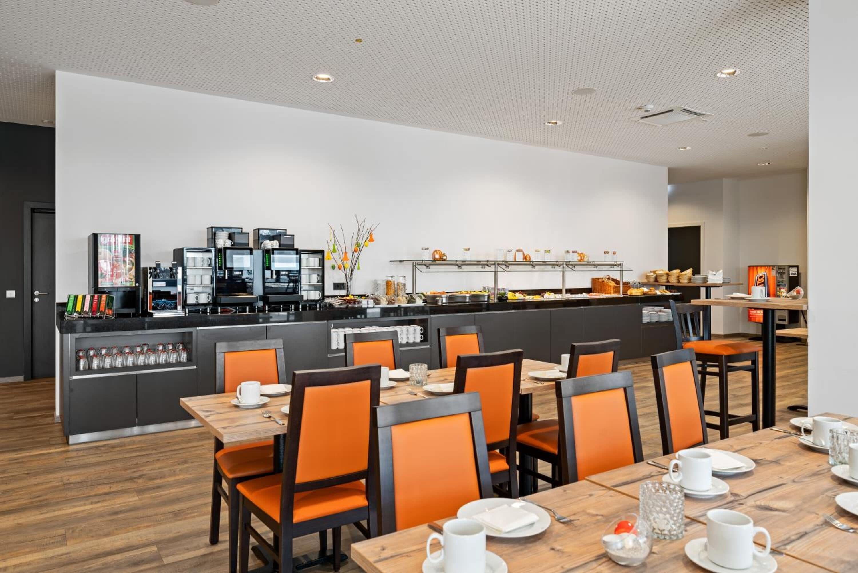 A modern dining area with multiple tables and chairs, a coffee station, and a buffet with various food items.