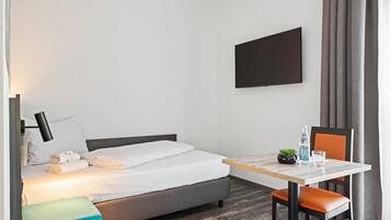 Habitación de hotel con cama, escritorio, silla, televisor y ventana con cortinas.