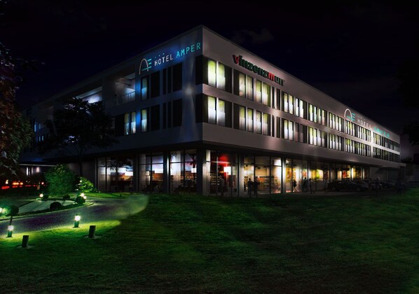 Un hotel moderno con varios pisos y fachada de vidrio, con señalización iluminada y un área de entrada bien iluminada.