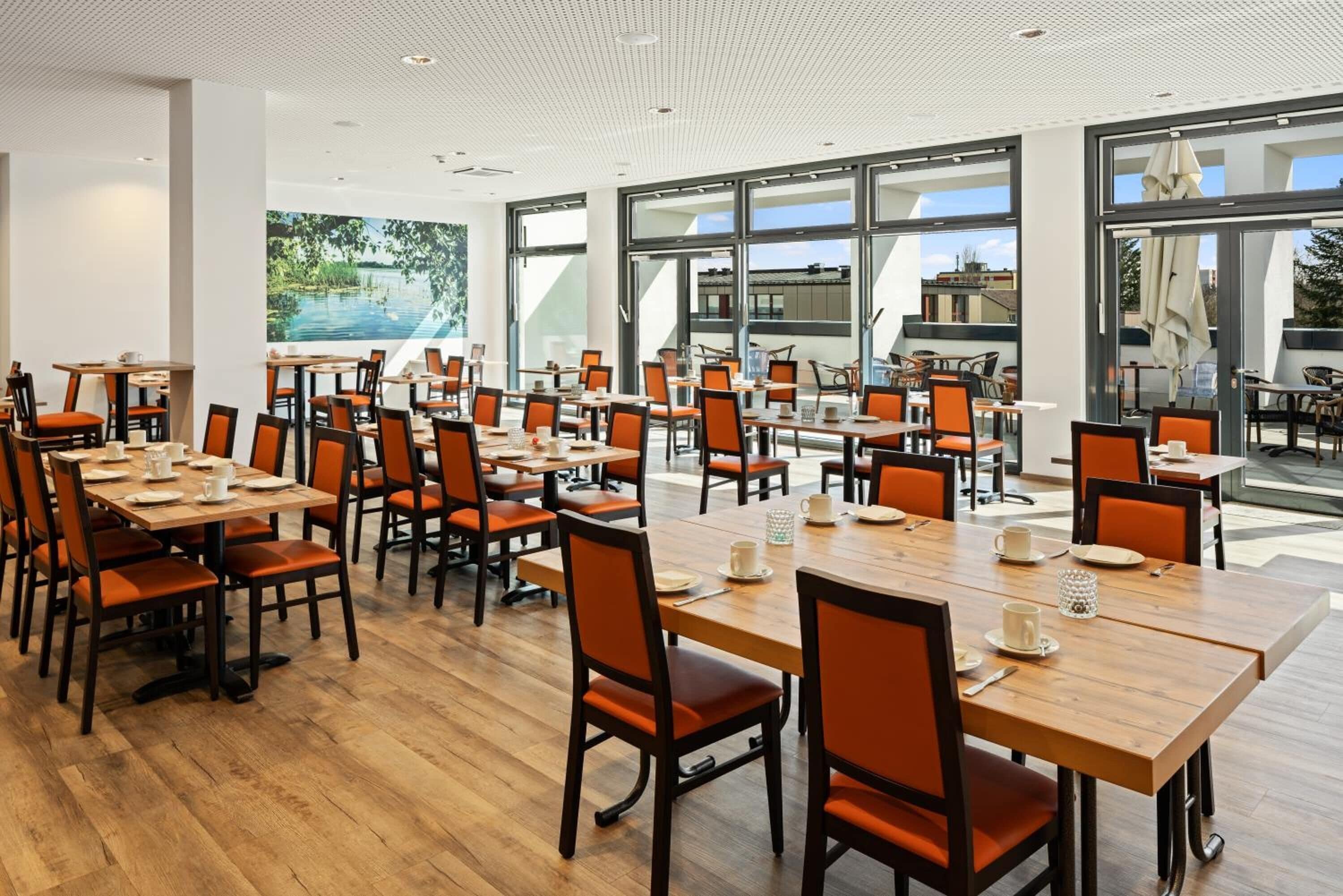 Ein geräumiger Essbereich mit mehreren Tischen und Stühlen, große Fenster mit Blick ins Freie und ein modernes Decken-Design.
