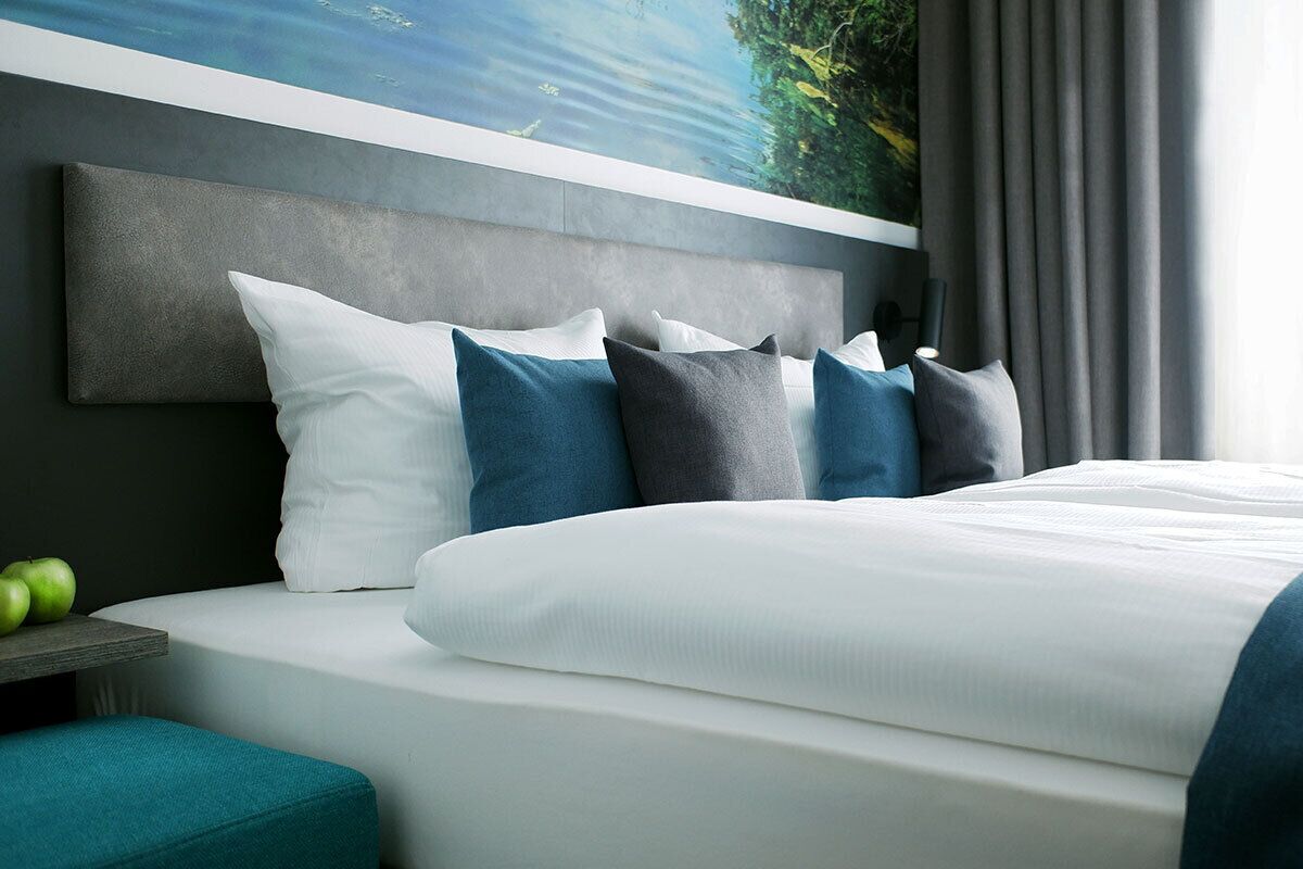 Ein modernes Hotelzimmer mit einem großen Bett, einer Kopfteil und Blick auf ein Gewässer durch ein Fenster.