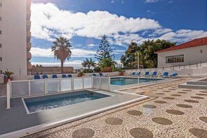 Un área de piscina en la azotea con dos piscinas, sillones de descanso y suelo de baldosas.