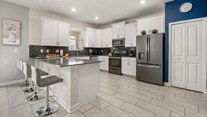 Una cocina moderna con armarios blancos, electrodomésticos de acero inoxidable y una isla central con taburetes de bar.