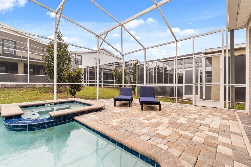A pool area with a glass enclosure, lounge chairs, and a hot tub.