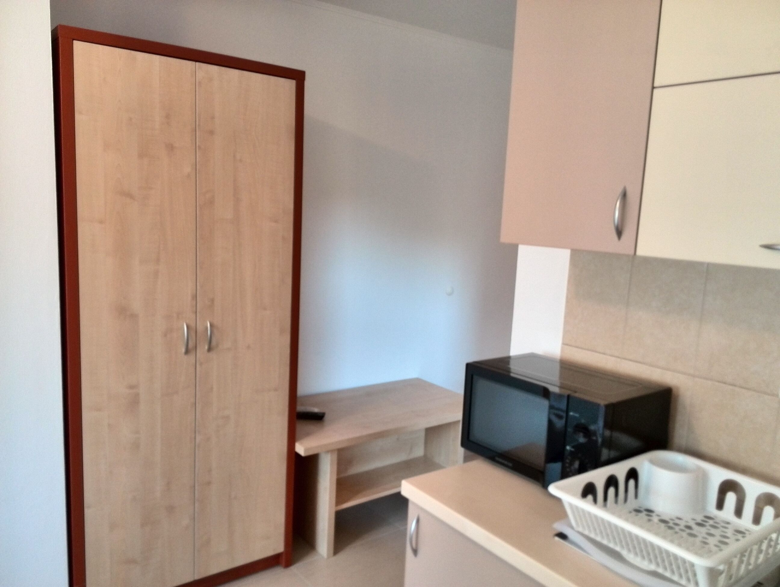 Eine kleine Küchenzeile mit einer Mikrowelle, einem Korb und einem Holzschrank.