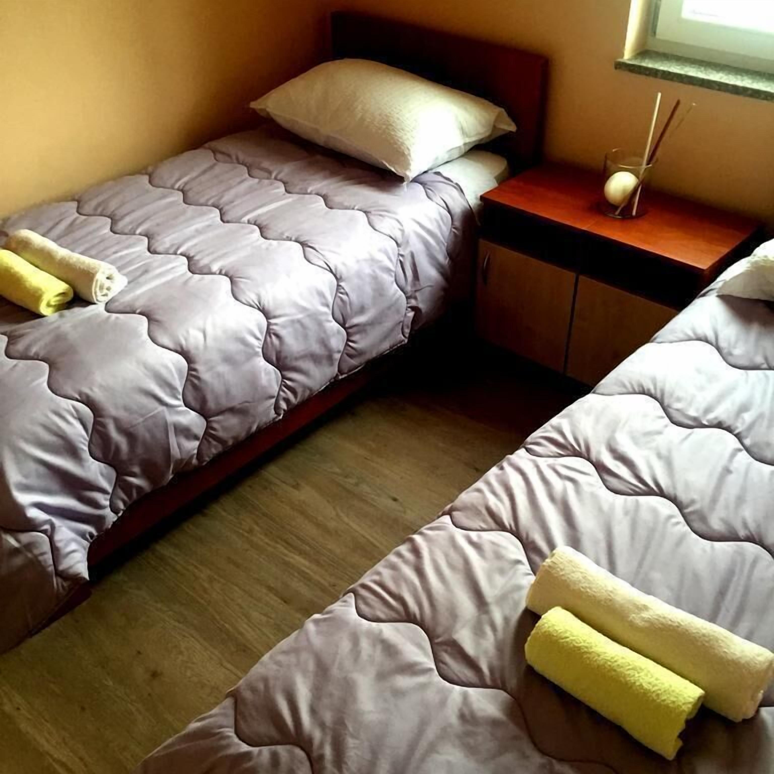 Une chambre avec deux lits, chacun doté d’une tête de lit, d’une table de chevet et d’une petite table de nuit avec une lampe.