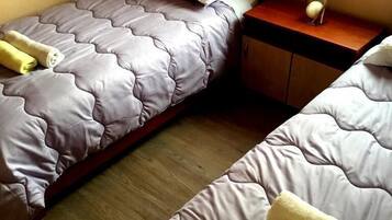 Une chambre avec deux lits, chacun doté d’une tête de lit, d’une table de chevet et d’une petite table de nuit avec une lampe.