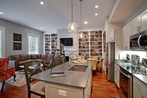 A modern kitchen with a central island, built-in shelves, and a dining area with a sofa and chairs.