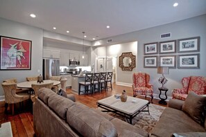 A spacious living area with a sofa set, a coffee table, and a dining table with chairs. There is a kitchen in the background with modern appliances. - Rare & Beautifully Updated 9 Bed, 8 Bath Townhome (Savannah)