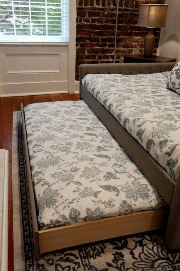 A bed with floral bedding in a room with a brick wall and a window with blinds.