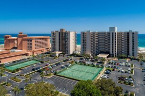 A high-rise hotel complex with multiple buildings, a parking lot, and a tennis court. - Orange Beach Alabama, 1 Bedroom Phoenix East 22102 (Orange Beach)