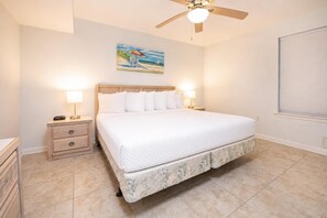 A bedroom with a bed, nightstands, a ceiling fan, a painting, and a window with blinds. - Orange Beach Alabama, 1 Bedroom Phoenix East 22102 (Orange Beach)