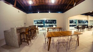 Un vaste espace dédié à la salle à manger, avec une grande table et des chaises en bois, un coin bar avec des tabourets, et de grandes fenêtres offrant une vue sur le paysage urbain.