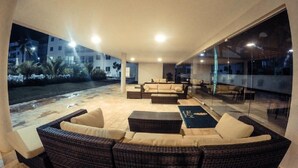 Un espace de vie extérieur moderne, doté de meubles en osier et d’un mur de verre donnant sur un jardin aménagé.
