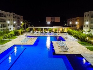 Une piscine divisée en deux zones distinctes, entourée de chaises longues et de palmiers.