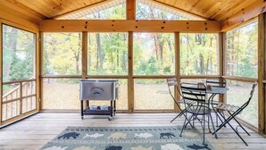 A covered outdoor area with a wooden ceiling, large windows, a barbecue grill, and a table with chairs. - DD Ranch - Newly Renovated 10-Person Home! (Union Pier)