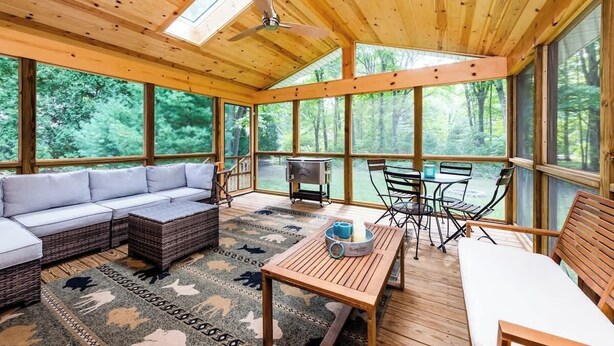 A wooden cabin with a large glass window, a ceiling fan, a sofa, a table, and a grill. - DD Ranch - Newly Renovated 10-Person Home! (Union Pier)