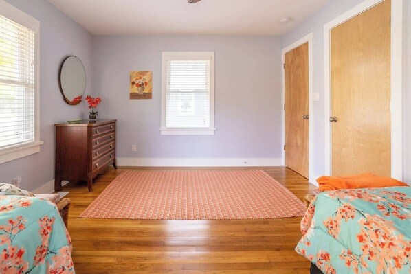 Une chambre avec deux lits, une commode, un miroir et une fenêtre avec des stores.