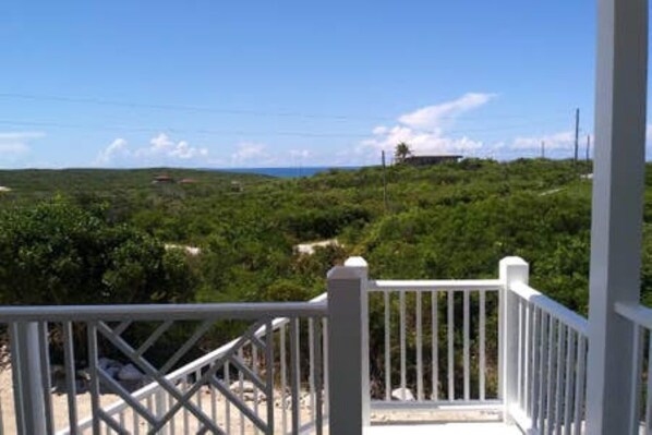 A white wooden deck with a metal railing overlooking a lush green landscape and a clear blue sky.