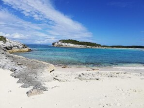 A beach with white sand, clear turquoise water, and rocky outcrops.