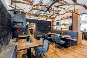 Un restaurante moderno con vigas de madera a la vista, paredes de piedra oscura y diferentes opciones de asientos, como mesas y cabinas.