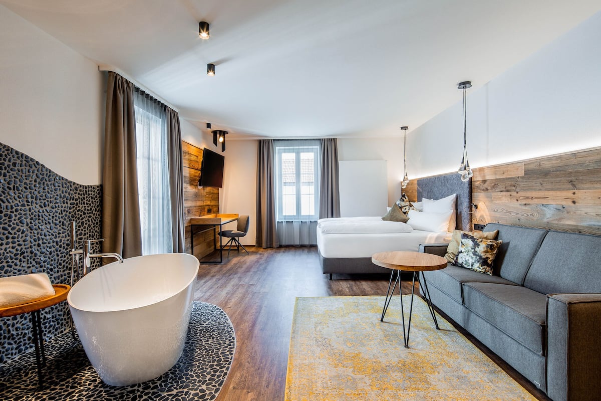 Une chambre d’hôtel moderne équipée d’une grande baignoire, d’un canapé, d’un bureau et d’un lit.