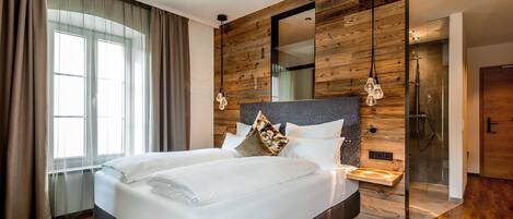 Una habitación de hotel moderna con una cama grande, panel de pared de madera y ducha integrada.