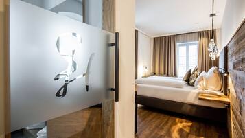 Quarto de hotel moderno com cama, piso de madeira e uma grande janela com cortinas.