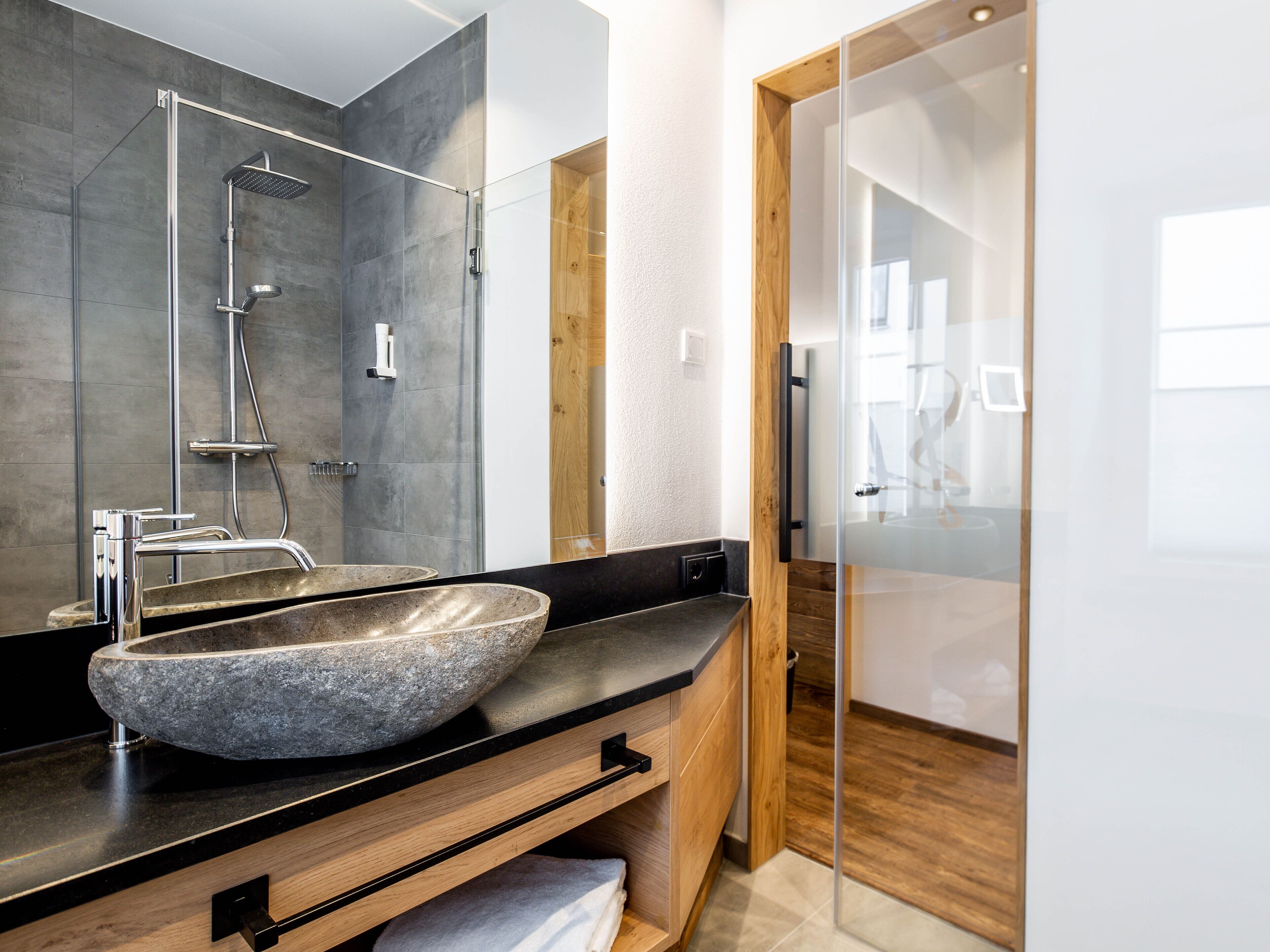 A modern bathroom with a large stone sink, a glass shower enclosure, and a wooden door.
