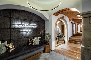 Un interior moderno con un sofá oscuro y texturizado, un letrero en la pared que dice 'Stempelberger Haus' y una escalera de madera que sube a otro nivel.