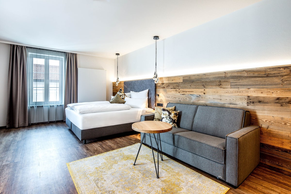 Une chambre moderne avec un lit, un canapé, une petite table ronde et un mur d’accent en bois.