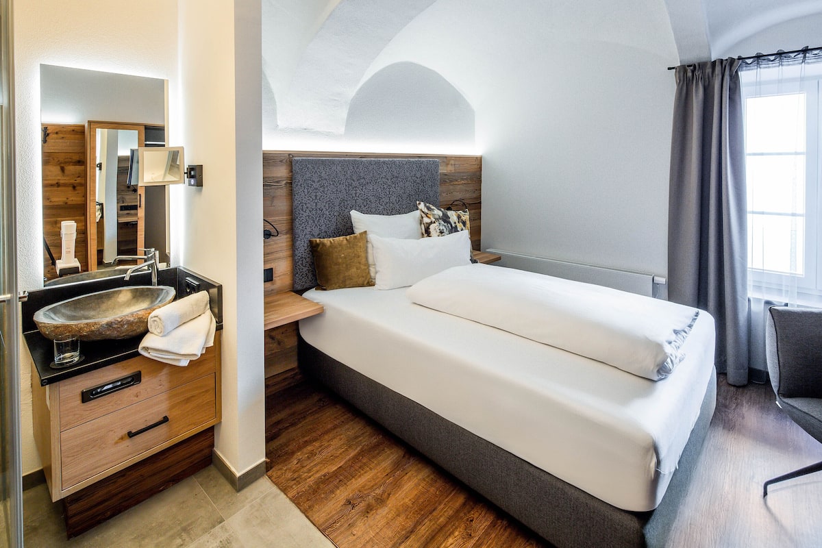 Une chambre d’hôtel moderne dotée d’un grand lit, d’une coiffeuse en bois, d’un lavabo intégré et offrant une vue sur l’extérieur.