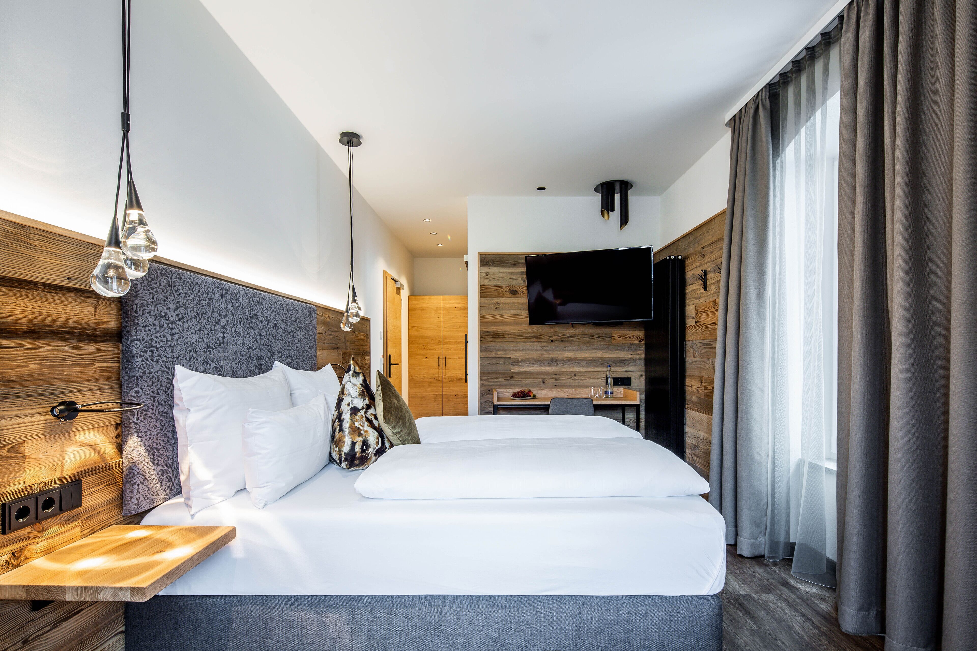 A modern hotel room with a large bed, a wooden headboard, a TV, and a desk with a chair.