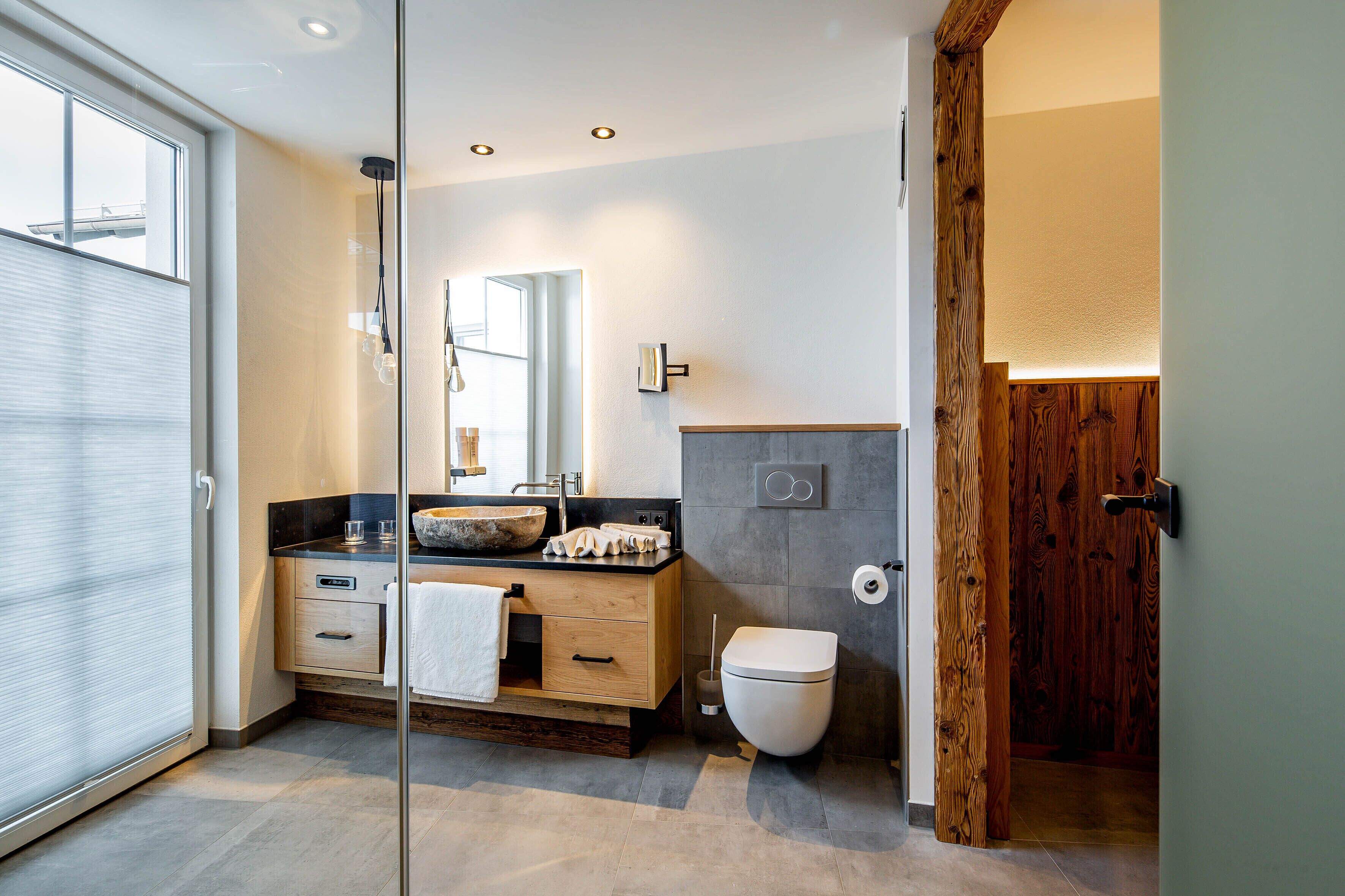 A modern bathroom with a wooden vanity, a large mirror, and a glass shower enclosure.