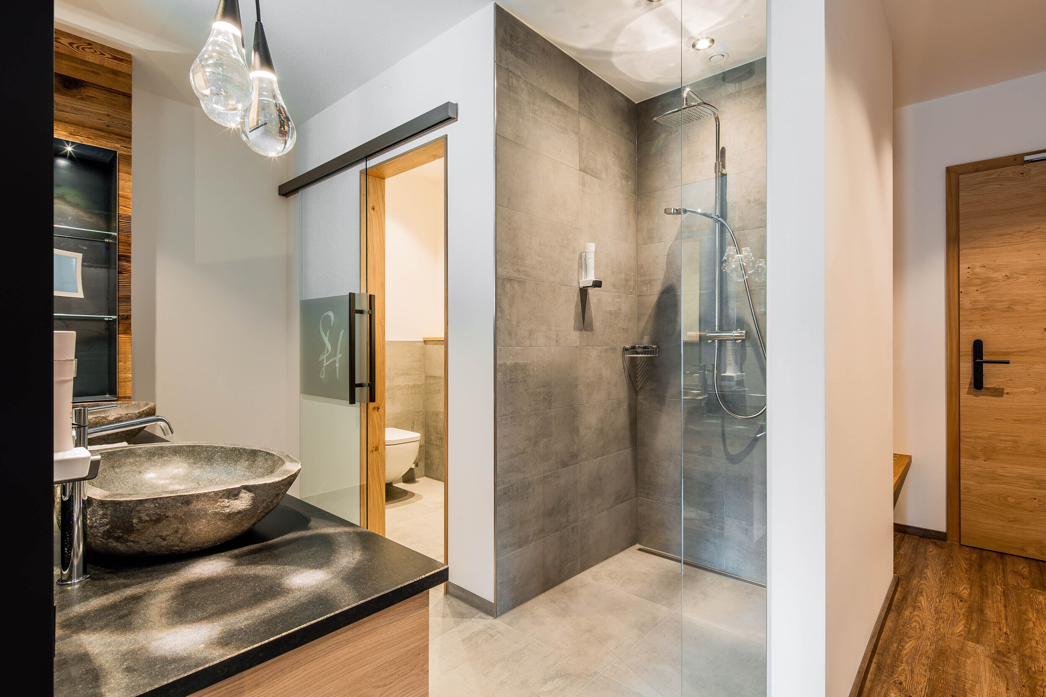 A modern bathroom with a large stone basin, a glass shower enclosure, and a wooden door.