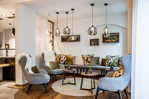 Una sala de estar moderna con un conjunto de sofá, dos sillones y una mesa de centro. Hay lámparas colgantes del techo y una mesita auxiliar con una planta.