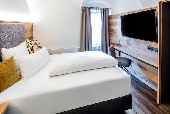 Habitación de hotel con una cama grande, un televisor de pantalla plana montado en una pared de madera y una ventana con cortinas.