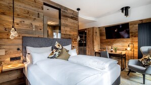 A modern hotel room with a wooden wall, a large bed, a desk, and a TV. - Stemplinger Hansl (Hauzenberg)