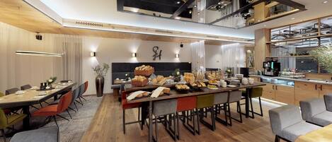 A modern kitchen with a central island, wooden cabinetry, and a dining area with a high ceiling and exposed beams.